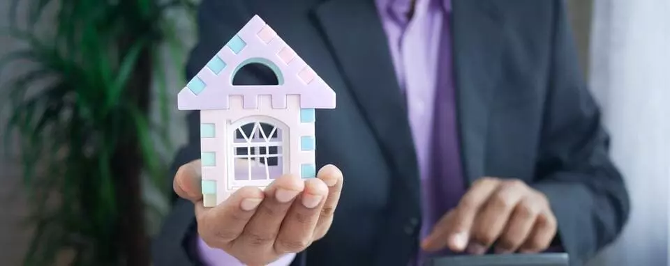 homem de terno segurando uma casa de brinquedo