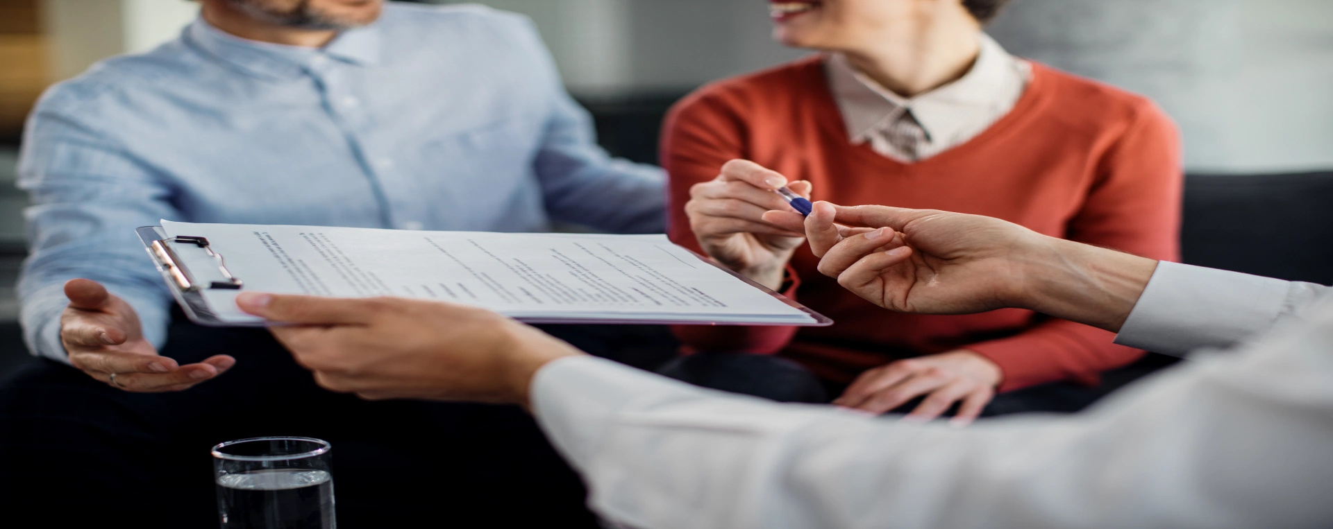 Foto de casal desfocado, assinando contrato de imóvel com um advogado especializado em direito imobiliário.